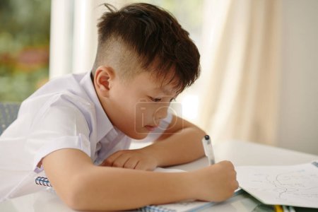 Téléchargez les photos : Un écolier vietnamien écrit dans un manuel au bureau en classe - en image libre de droit