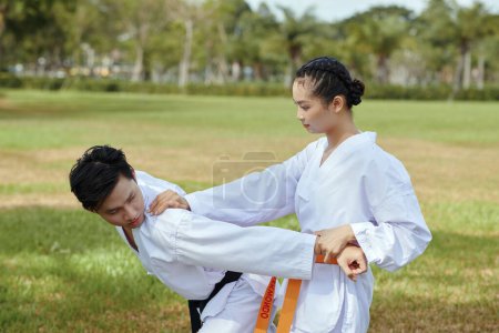 Photo for Taekwondo athlete attacking her opponent when fighting outdoors - Royalty Free Image