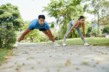 Téléchargez les photos : S'adapter jeune couple échauffement et étirement des jambes avant de courir dans le parc - en image libre de droit