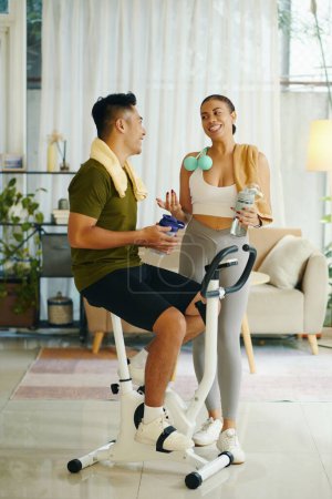 Photo for Sporty couple drinking water and chatting after working out together at home - Royalty Free Image