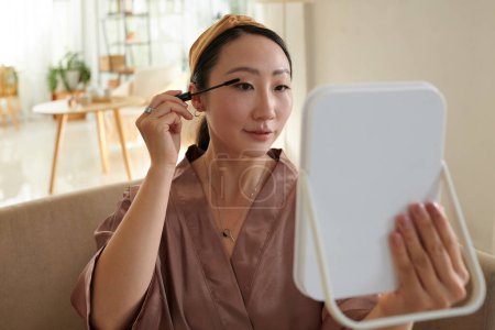 Portrait of Chinese young woman applying volumizing black mascara