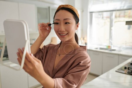 Happy woman applying lengthening mascara when getting ready