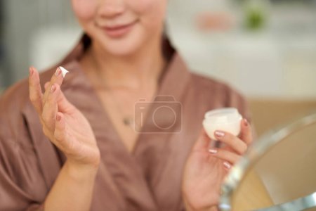 Photo for Young woman in satin robe applying anti-aging night cream - Royalty Free Image