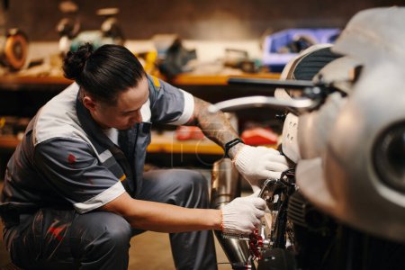 Téléchargez les photos : Mécanicien en uniforme fixation moto cassée du client - en image libre de droit