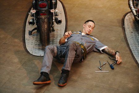 Photo for Mechanic choosing wrench when repairing motorcycle in workshop - Royalty Free Image