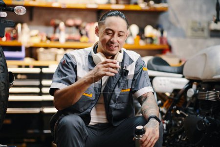 Photo for Portrait of smiling mechanic drinking coffee from thermos during break - Royalty Free Image