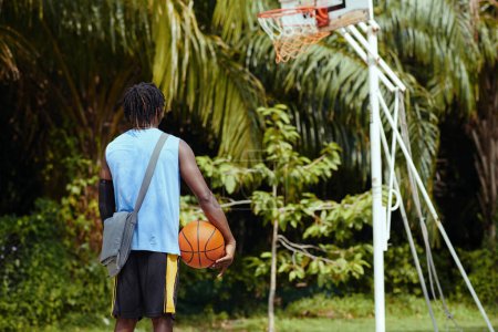 Foto de Deportista pensativo con pelota de baloncesto mirando a la cesta, vista desde la parte posterior - Imagen libre de derechos