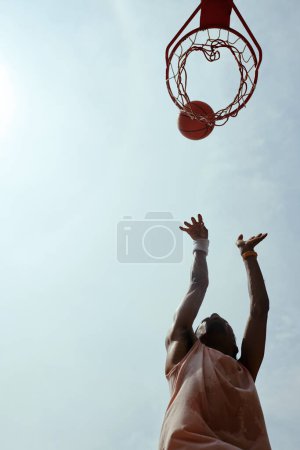 Foto de Atleta sudoroso lanzando pelota en la cesta, vista desde abajo - Imagen libre de derechos