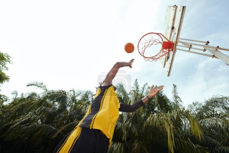 Photo for Player throwing ball in basket when playing outdoors, view from below - Royalty Free Image