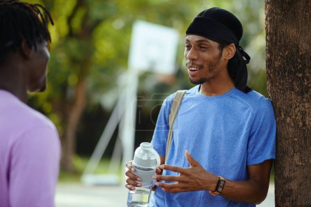 Téléchargez les photos : Joyeux homme noir boire de l'eau et parler à un ami après avoir payé ensemble à l'extérieur - en image libre de droit