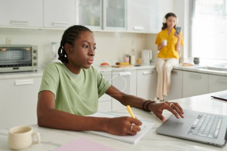 Téléchargez les photos : Étudiant noir travaillant sur ordinateur portable au comptoir de cuisine - en image libre de droit