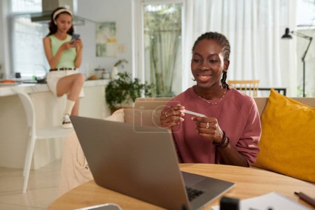 Foto de Sonriente chica negra limar las uñas al ver el espectáculo en el ordenador portátil en casa - Imagen libre de derechos