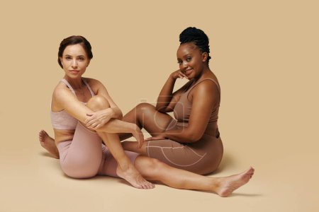 Foto de Sonriente ajuste delgado y curvas mujeres sentadas en el piso del estudio - Imagen libre de derechos