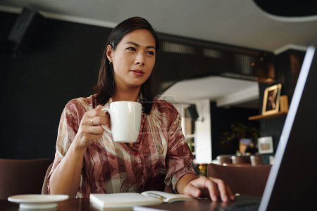 Téléchargez les photos : Femme d'affaires boire le café du matin et lire l'article de nouvelles sur ordinateur portable - en image libre de droit