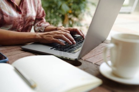 Téléchargez les photos : Image rapprochée de la femme travaillant sur un ordinateur portable à une table de café extérieure - en image libre de droit