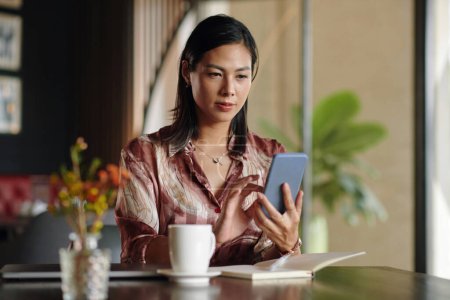 Photo for Businesswoman sitting at cafe table, checking emails on smartphone and writing in planner - Royalty Free Image