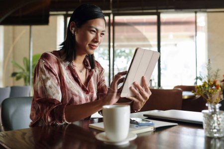 Téléchargez les photos : Femme d'affaires joyeuse assise à la table du café et regardant la présentation du produit sur tablette - en image libre de droit
