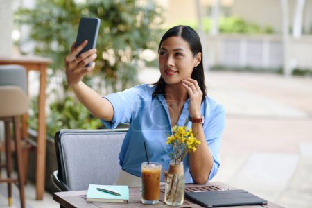 Téléchargez les photos : Femme d'affaires vietnamienne souriante prenant selfie à la table de café extérieure - en image libre de droit