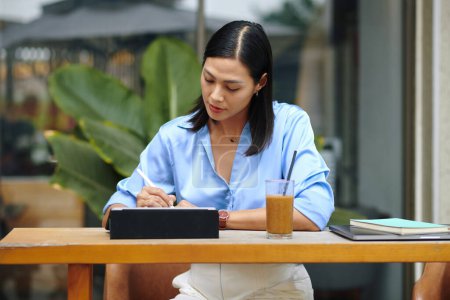 Téléchargez les photos : Femme d'affaires signant des documents sur tablette lorsque vous travaillez à la table de café - en image libre de droit