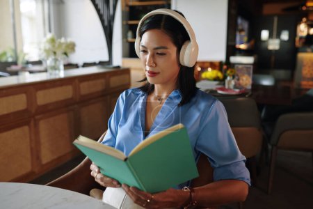 Téléchargez les photos : Femme assise à la table du restaurant écoutant de la musique calme dans les écouteurs et planificateur de lecture - en image libre de droit