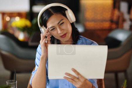 Photo for Smiling creative Vietnamese woman in headphones looking at her drawing - Royalty Free Image