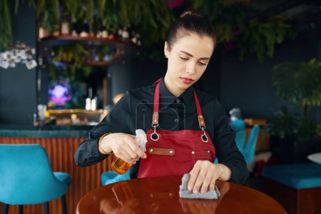 Téléchargez les photos : Serveur essuyant tables de restaurant avec pulvérisation désinfectante - en image libre de droit