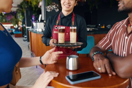 Foto de Camarero trayendo café helado a la pareja en la mesa del restaurante - Imagen libre de derechos