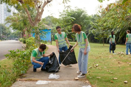Foto de Grupo de estudiantes en chalecos limpiando el parque local de la basura - Imagen libre de derechos