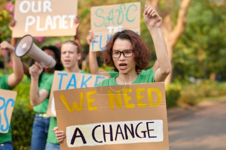 Téléchargez les photos : Éco-activiste criant en participant à une manifestation, marchant avec une pancarte - en image libre de droit