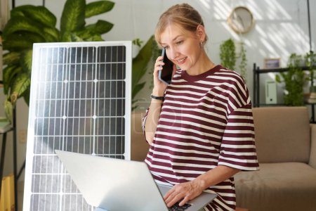 Photo for Smiling woman calling to client service to get information on how to change broken solar panel - Royalty Free Image