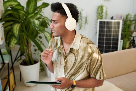 Foto de Hombre contemplativo escuchando podcast sobre energía solar y tomando notas - Imagen libre de derechos
