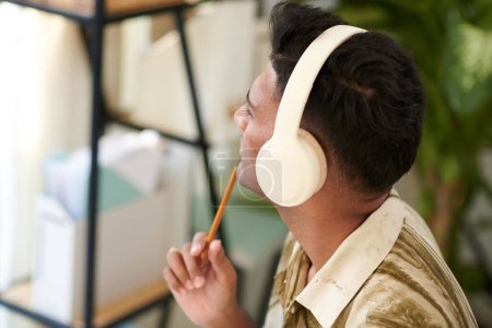 Téléchargez les photos : Homme pensif dans les écouteurs écoutant podcast et prenant des notes - en image libre de droit