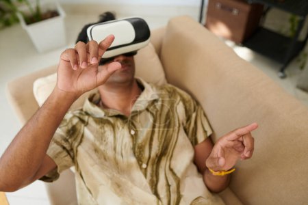 Téléchargez les photos : Homme en réalité virtuelle casque couché sur le canapé et jouer au jeu vidéo ou de travail - en image libre de droit
