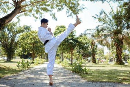 Téléchargez les photos : Athlète actif de taekwondo portant le dobok en faisant le coup haut - en image libre de droit