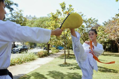 Photo for Taekwondo athlete kicking pad in hands of sportsman - Royalty Free Image