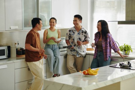 Téléchargez les photos : Des gens joyeux debout dans la cuisine, prenant des boissons et discutant de nouvelles - en image libre de droit