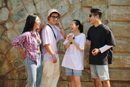 Téléchargez les photos : Groupe d'amis joyeux riant en se tenant debout au mur de pierre - en image libre de droit