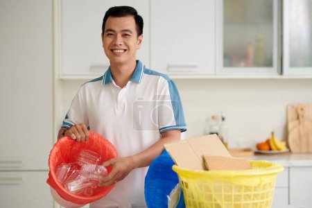 Foto de Retrato del hombre vietnamita sonriente clasificando residuos en casa - Imagen libre de derechos