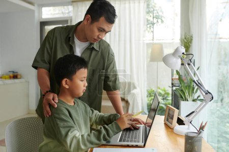 Téléchargez les photos : Père aidant fils préadolescent travaillant sur ordinateur portable - en image libre de droit