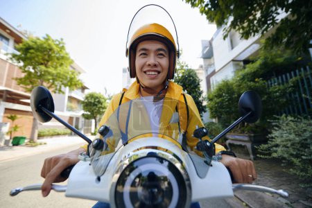 Photo for Excited Vietnamese young man riding motorbike delivering food to customers - Royalty Free Image