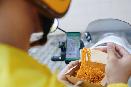 Foto de Conductor de taxi moto comprobar las solicitudes en el teléfono inteligente al comer el almuerzo - Imagen libre de derechos
