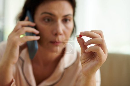 Foto de Mujer enferma mirando píldora cuando llama al médico - Imagen libre de derechos