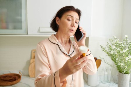 Foto de Mujer madura enferma en pijama de satén llamando al médico para hablar de medicina - Imagen libre de derechos