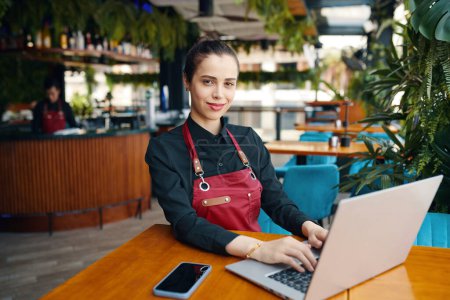 Téléchargez les photos : Portrait de gérant de restaurant souriant travaillant sur ordinateur portable - en image libre de droit