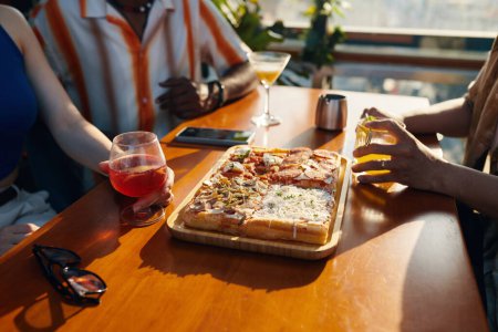 Téléchargez les photos : Image rapprochée d'amis mangeant de la pizza et buvant des boissons en traînant dans un café - en image libre de droit