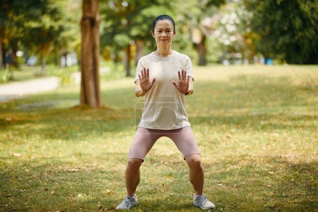 Photo for Smiling woman doing tai chi horse stance when breathing out outdoors - Royalty Free Image