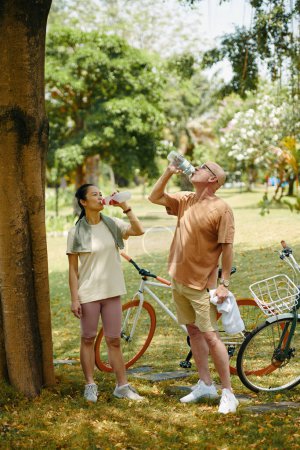 Foto de Sedienta pareja adulta bebiendo agua dulce después de montar en bicicleta - Imagen libre de derechos
