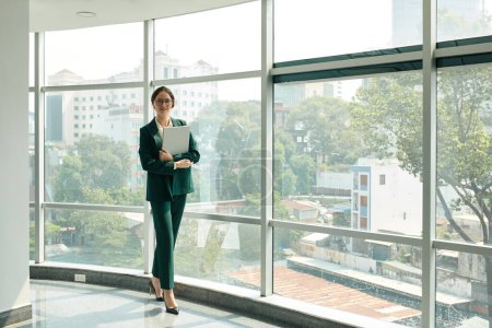 Foto de Retrato de mujer empresaria con portátil de pie en la ventana panorámica de la oficina - Imagen libre de derechos