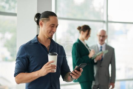 Lächelnder Geschäftsmann, der Kaffee trinkt und Texte von Kollegen beantwortet