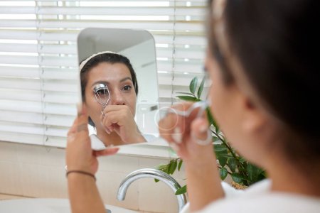 Woman looking at small mirror when curling lashes